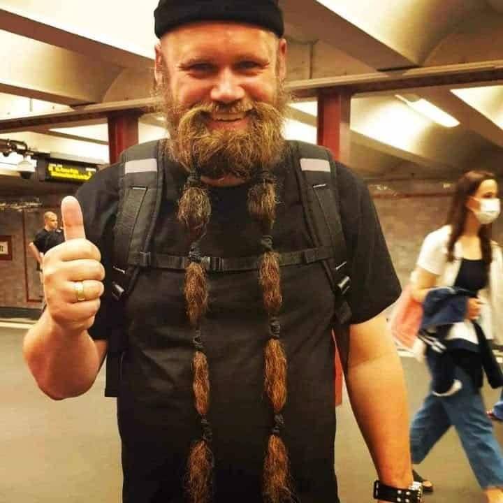 Glad mann med flettet skjegg i flere nivåer, står i undergrunnen og viser tommel opp.